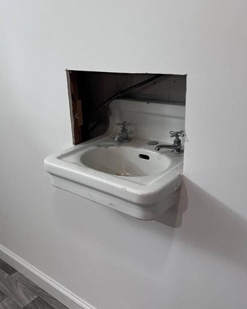 Small wall-mounted sink with two taps in a wall opening.