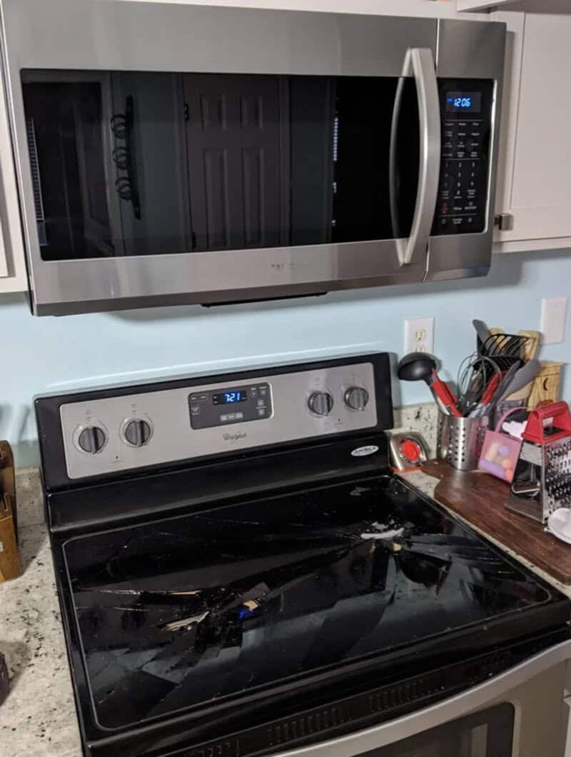 Microwave above a stove with a broken glass cooktop and scattered debris.