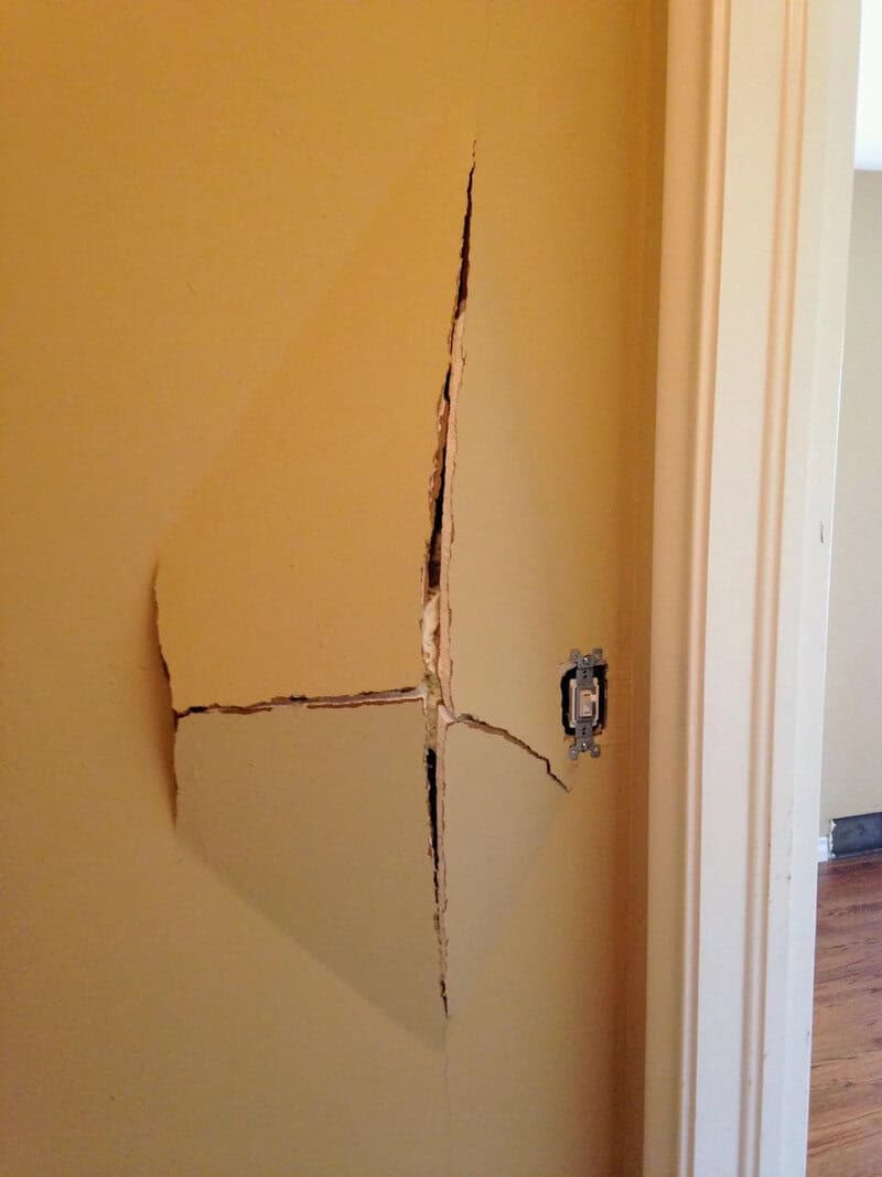 Large crack in yellow wall near door frame, with hole and electrical outlet.