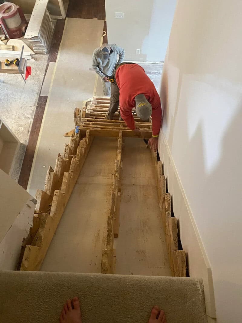 Two workers installing a staircase with a missing middle section.