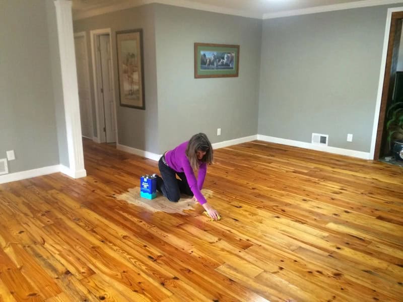 Woman cleaning a wooden floor in a living room.