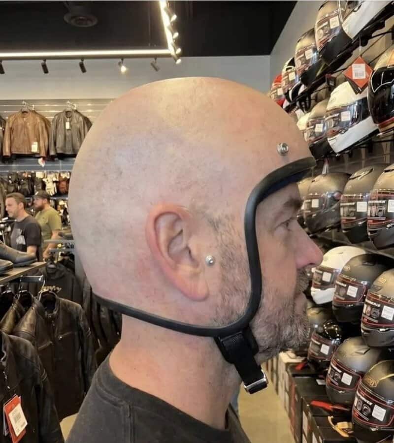 Man trying on a motorcycle helmet without a chin strap in a store.