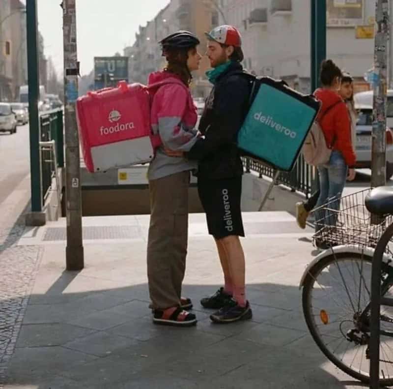 Foodora and Deliveroo delivery people face to face on the street.