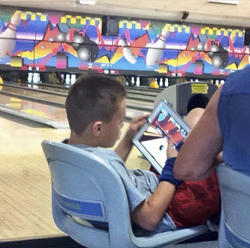Boy playing with a tablet at a bowling alley.