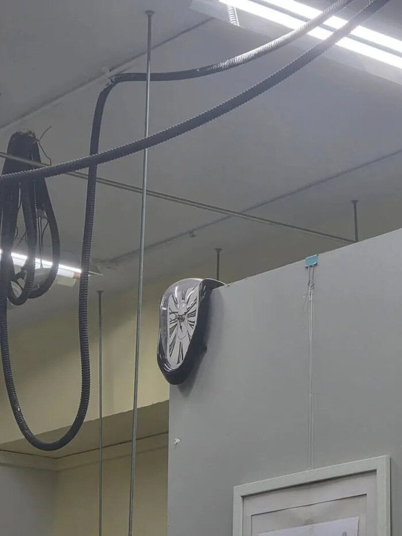 Clock with a distorted face hanging on a wall in an industrial setting.