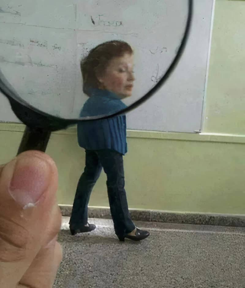Person holding magnifying glass in front of a woman walking in a classroom.