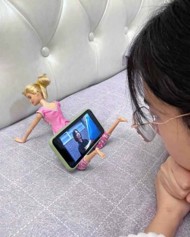 Girl watching a doll with a smartphone on the bed.