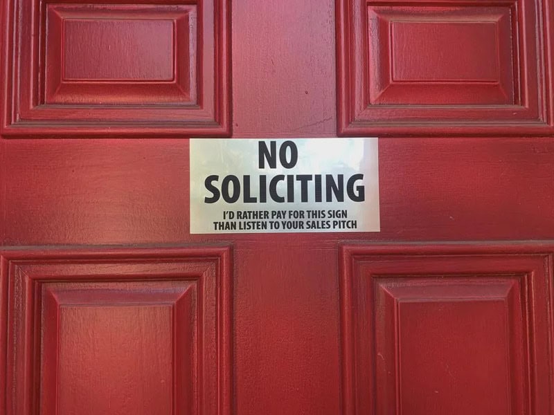 No Soliciting sign on a red door with additional text.
