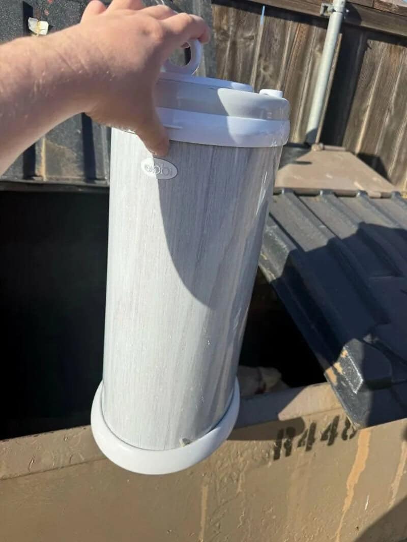 Person holding a white water filter pitcher outdoors with a wooden fence in the background.