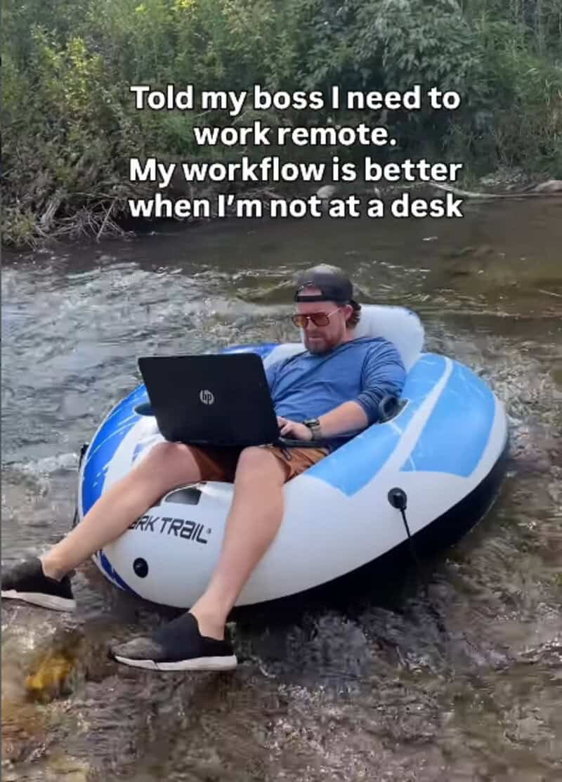 Man working remotely on a laptop in a boat on a river with trees.