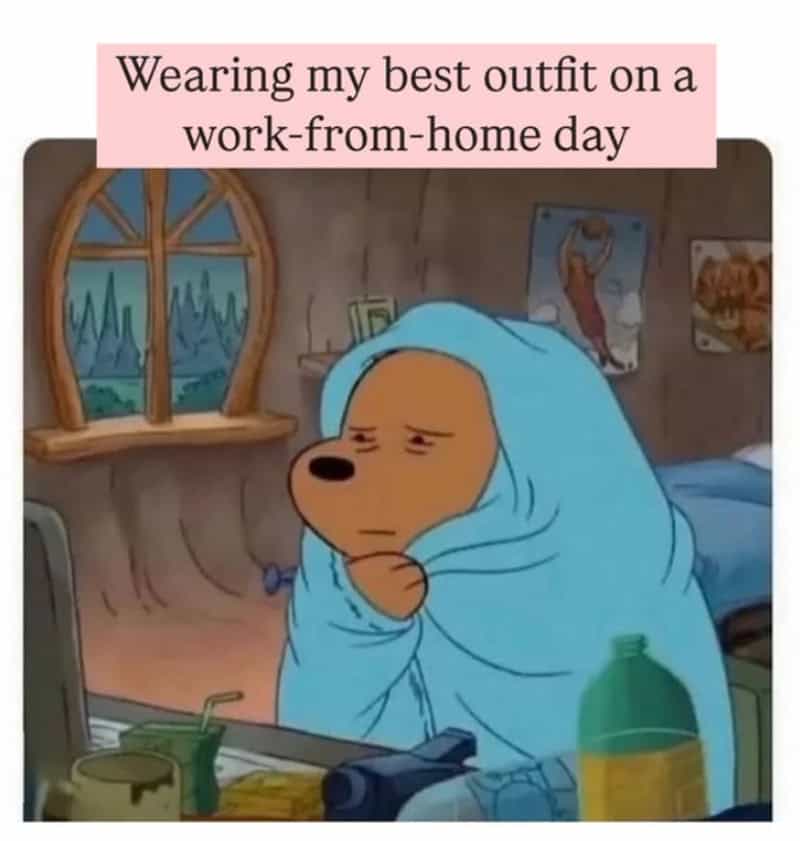 Dog wrapped in a blue blanket, sitting at a desk with a computer, looking tired.