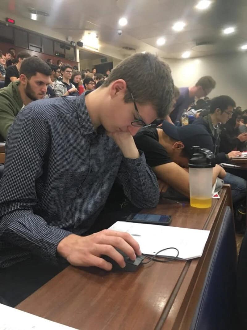Young man with glasses studying in a crowded lecture hall.