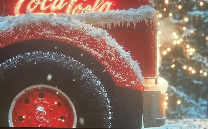 Close-up of a Coca-Cola truck with snow on it, Christmas lights in background.