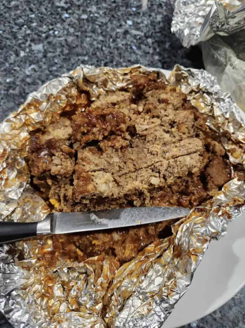 A partially eaten chocolate chip cookie in aluminum foil with a knife.