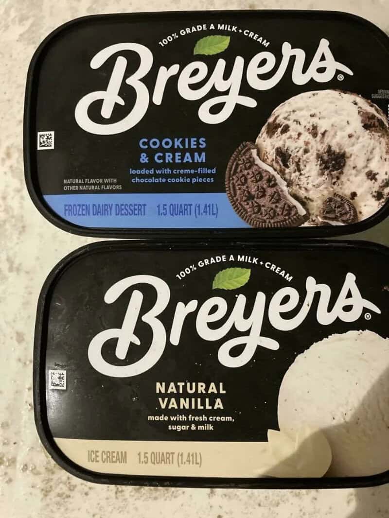 Two Breyers ice cream containers, cookies & cream and vanilla, on a black surface.