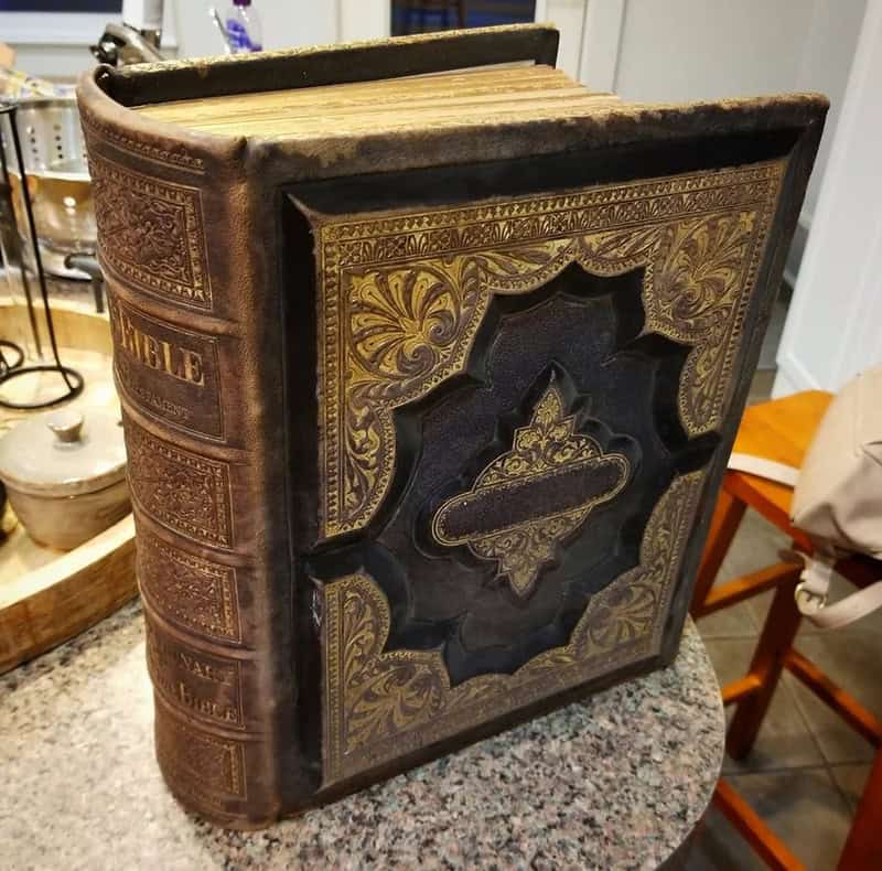 Old, ornate Bible with gold and black cover on a table.
