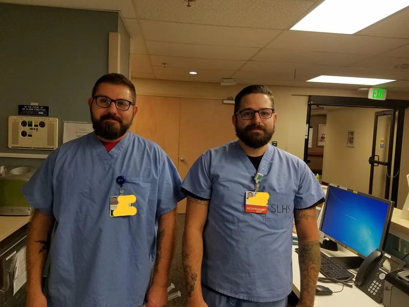 Two male healthcare workers in scrubs standing in a hospital room.