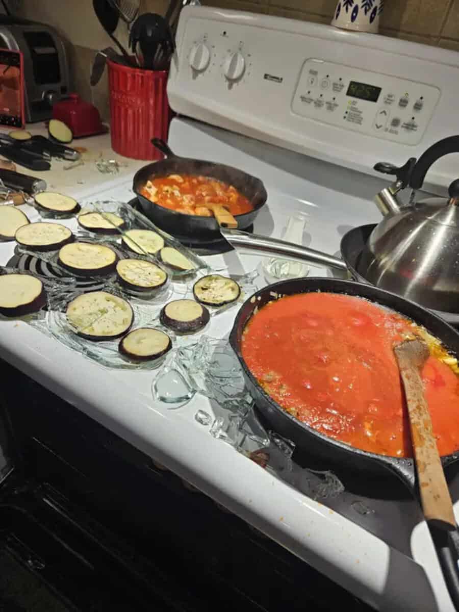 Eggplant slices cooking on a stove with tomato sauce in pans and eggplant slices on a tray.