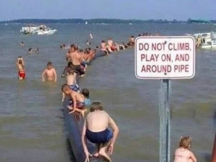 People on a pipe in the water with a sign that says 'Do not climb, play on, and around pipe'.