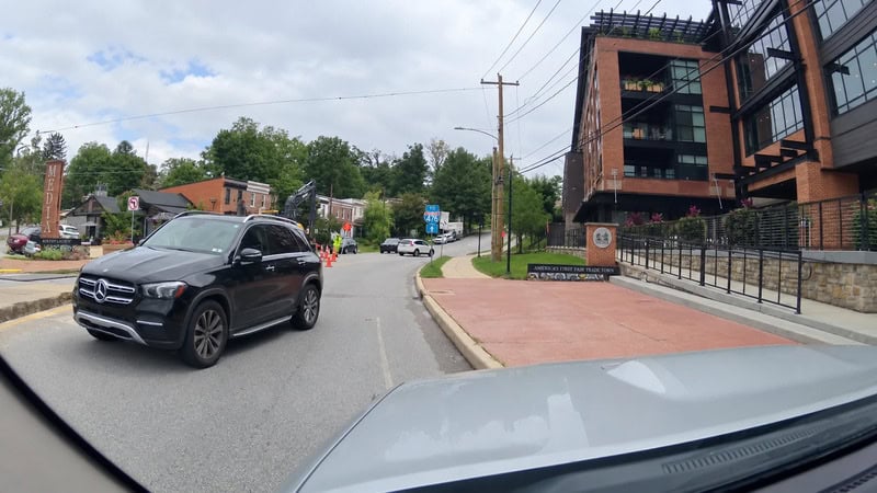 View of a street with a black Mercedes SUV and a gray car in front, modern building on the right, on.