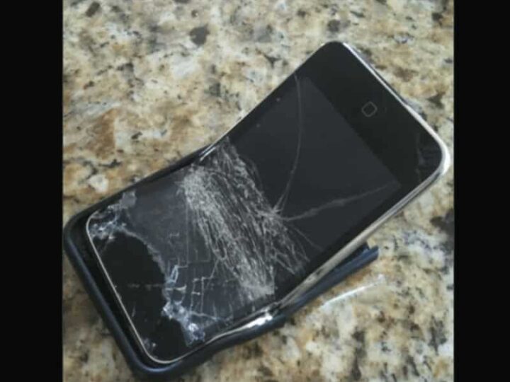 Broken flip phone on a granite surface with a cracked screen.