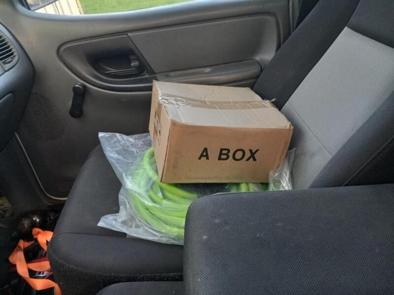 A cardboard box labeled 'A BOX' on a car seat with a plastic bag and green item inside.