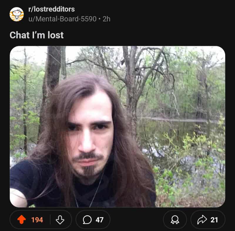A man with long hair and a serious expression in a wooded area.