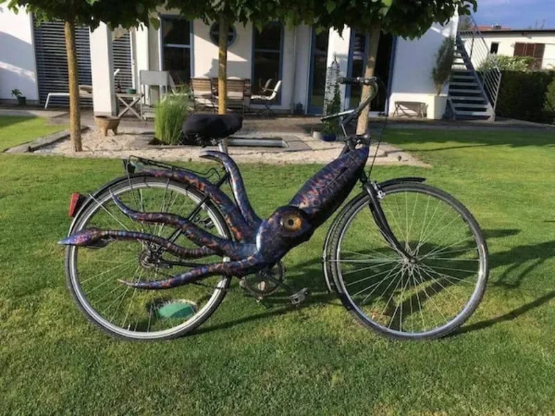 Bicycle with an octopus design painted on it, parked on grass.