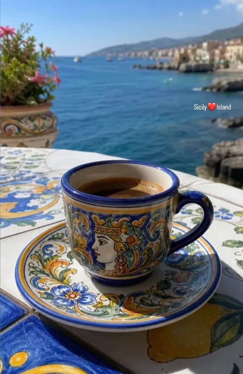 Coffee cup with colorful design on a table overlooking the sea in Sicily.