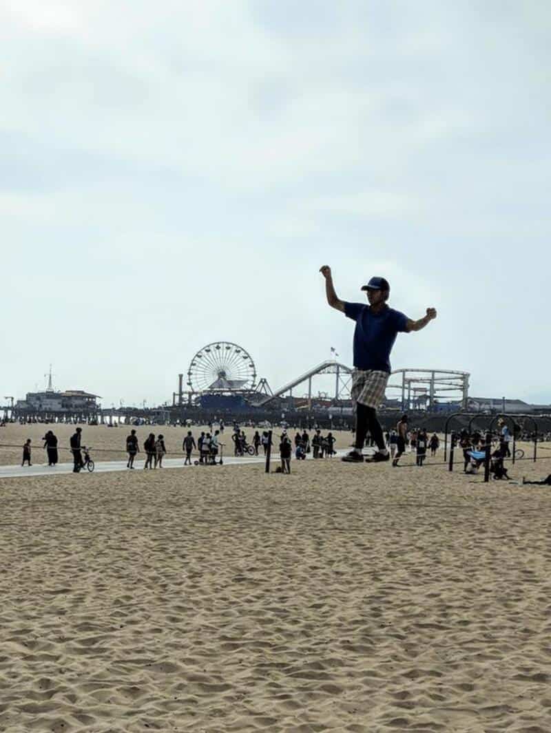 Giant person figure on the beach with a Ferris wheel in the background.