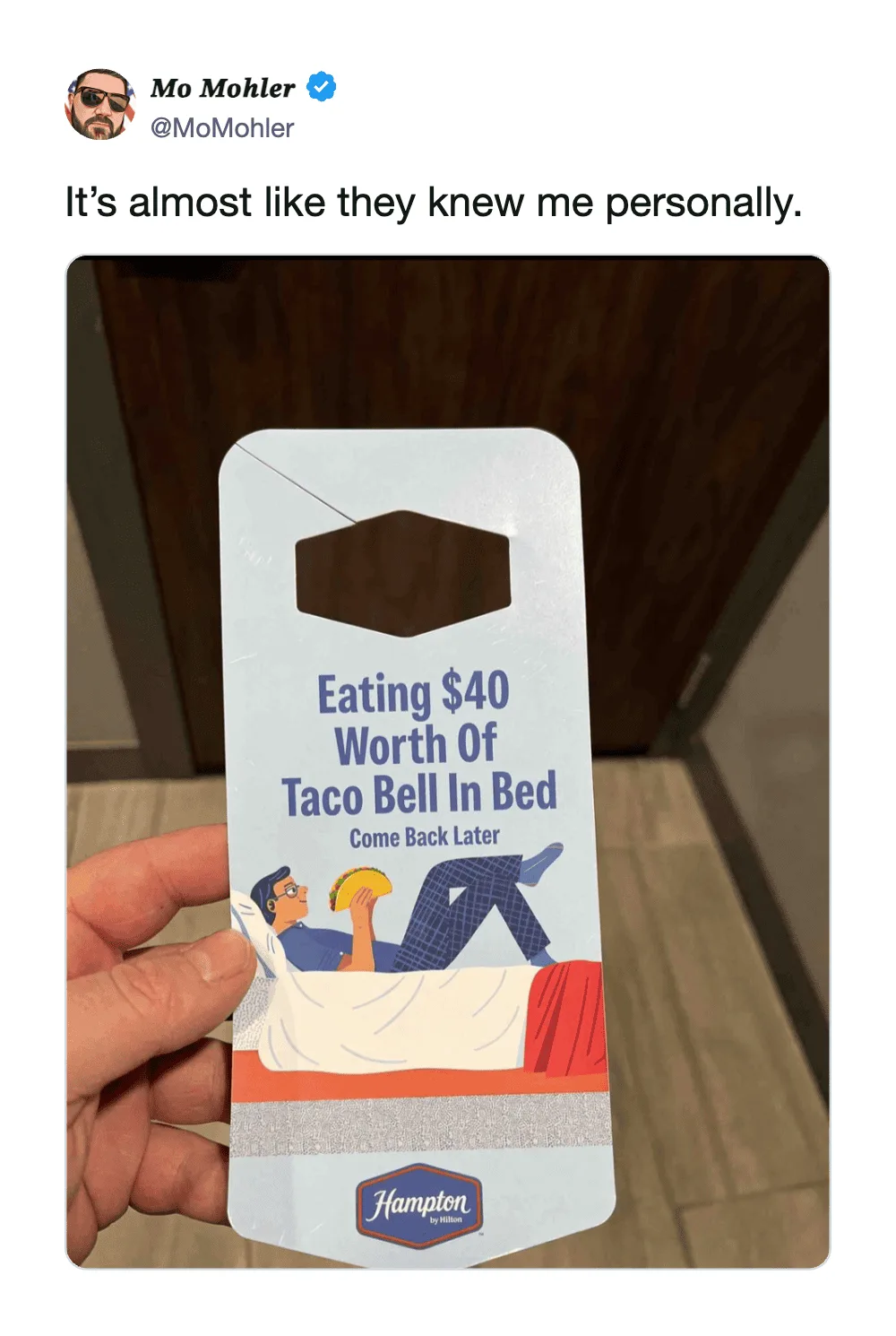 A person holding a Hampton Inn key card with a humorous message about Taco Bell.