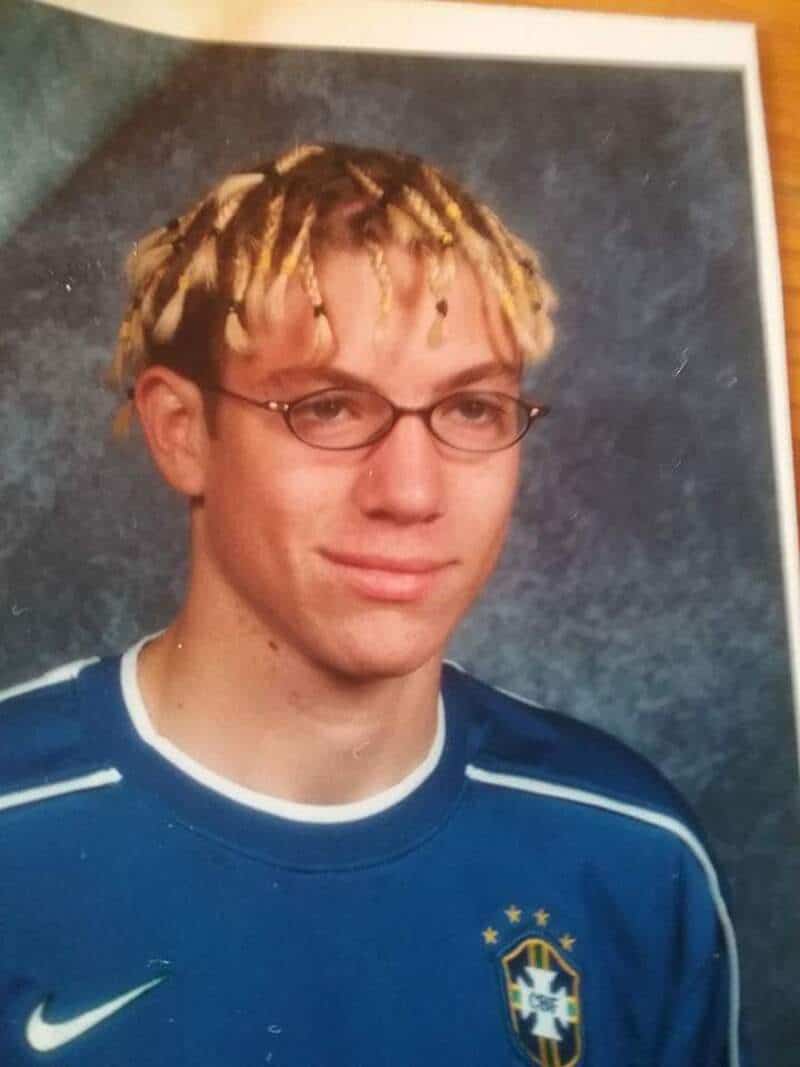 Young man with blond dreadlocks, glasses, and a blue sports jersey with a crest.