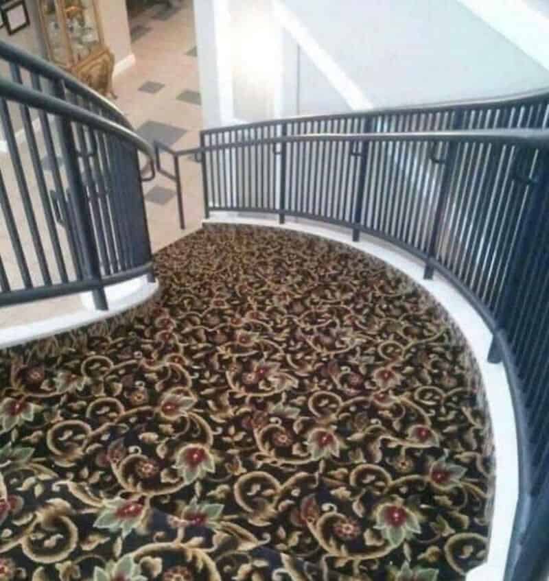 Curved staircase with ornate floral carpet and black metal railing in a shopping mall.