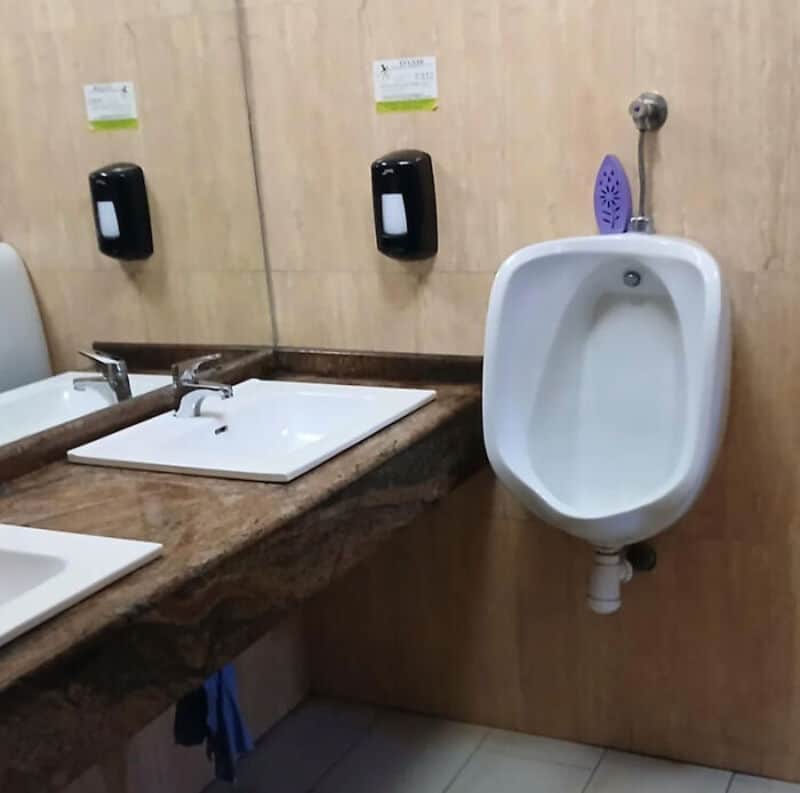Restroom with two sinks and a urinal, soap dispensers on the wall.