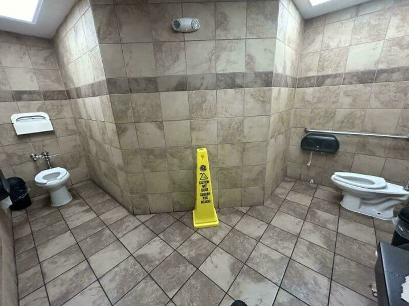 Public restroom with a yellow caution sign blocking the corner.