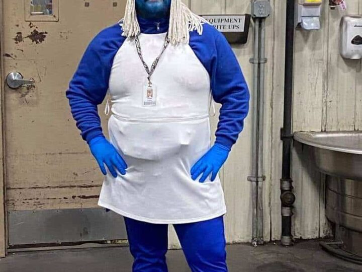Person dressed as a Smurf with blue face paint, white hair, and a white apron.