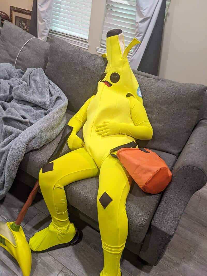 Person in Pikachu costume sitting on a couch with a bag and slippers.