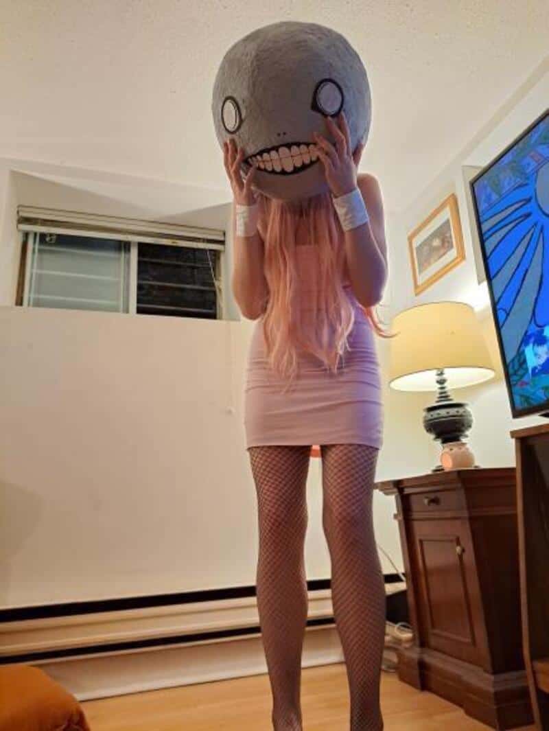 Person in pink dress with fishnet stockings holding a large cartoonish skull mask.