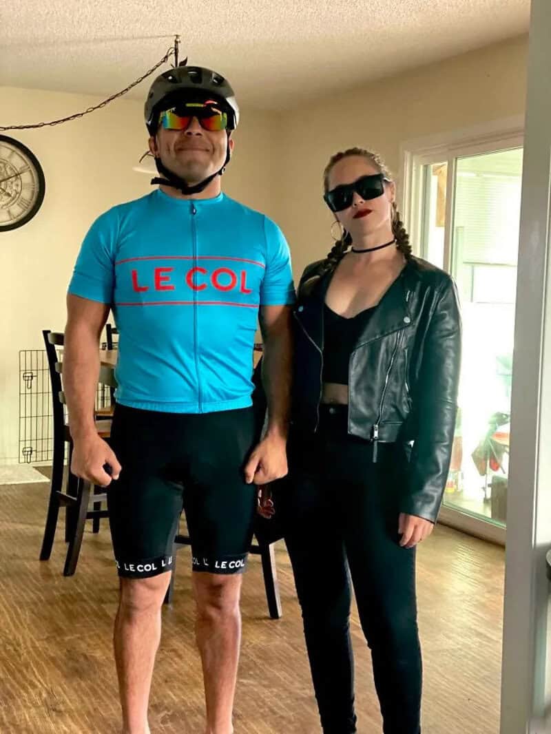 Two people in costumes, one in cycling gear, the other in a leather jacket and sunglasses.