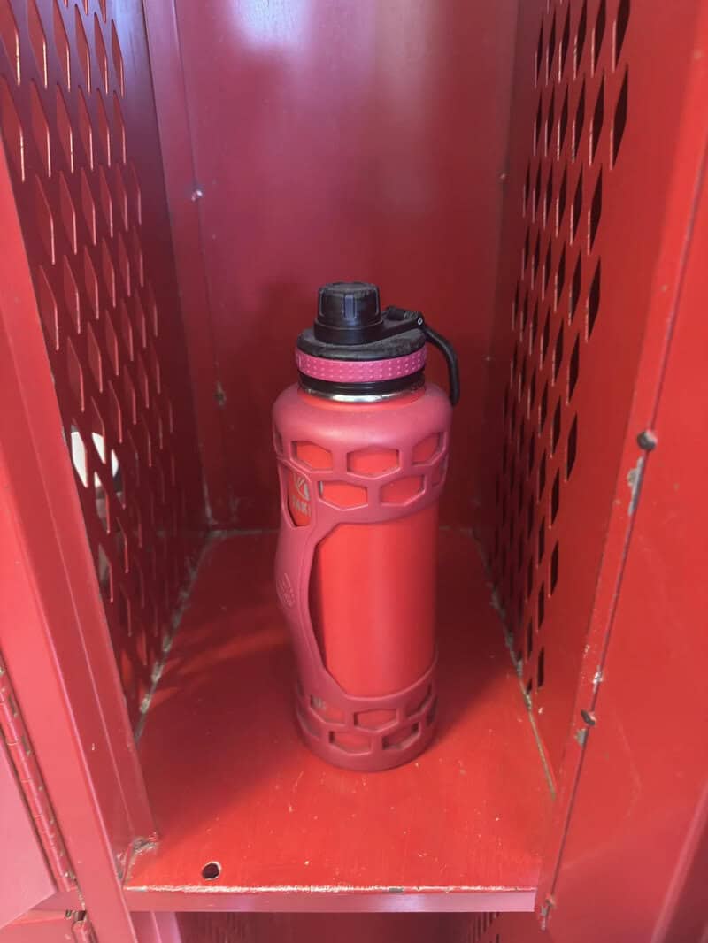 Red water bottle inside a red locker with ventilation holes.