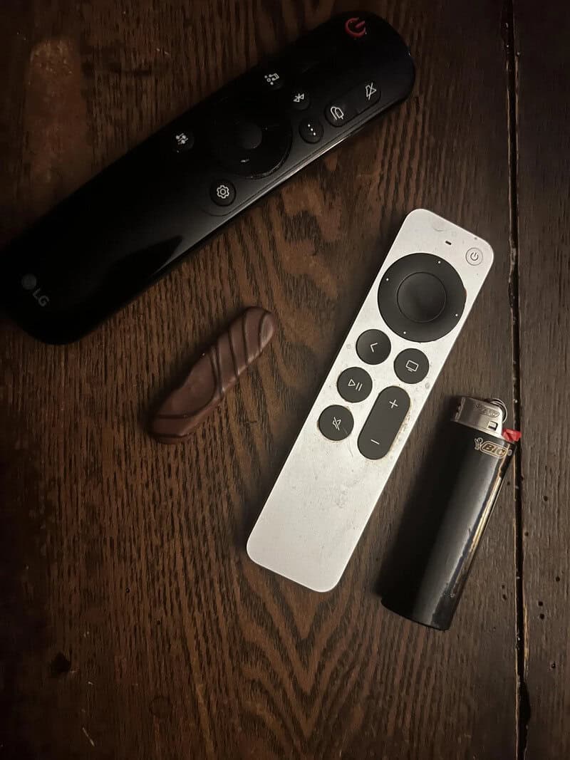 Remote controls, a chocolate, and a lighter on a wooden surface.