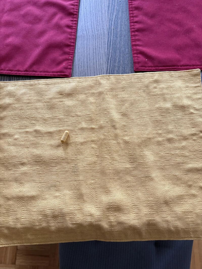 Close-up of a beige fabric bag with a small beige zipper pull on a dark surface.