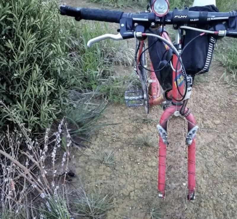 Close-up of a red mountain bike on a dirt trail with bushes on the side.