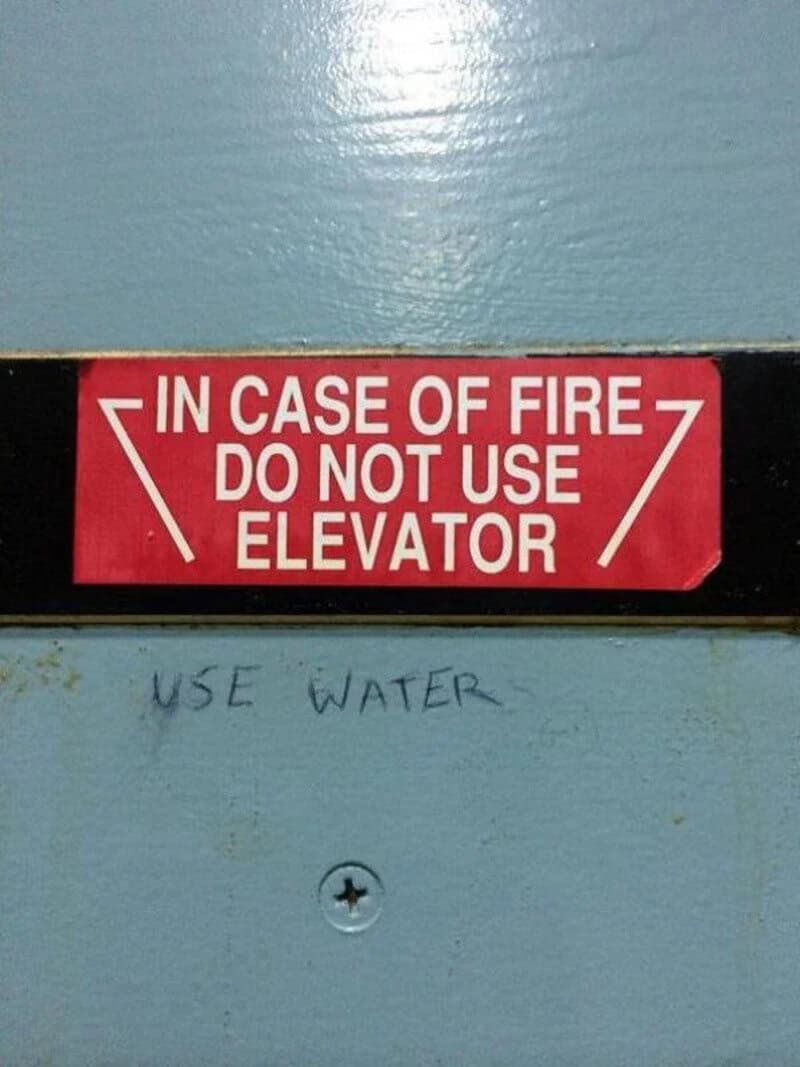 Red sign says 'In case of fire do not use elevator' with handwritten note below saying 'Use water'.