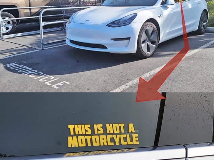 Car with a sign that says "This is not a motorcycle" in parking lot.