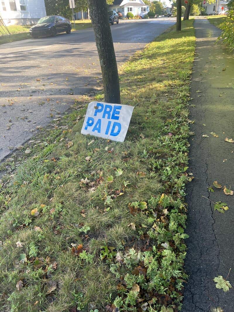 Sign on grass reads 'PRE PA ID' with a tree and sidewalk in the background.