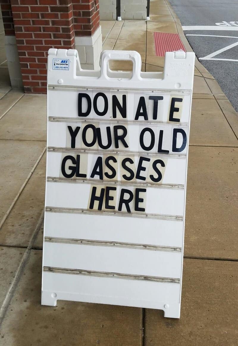 Signboard reading 'DONATE YOUR OLD GLASSES HERE' outside a building.