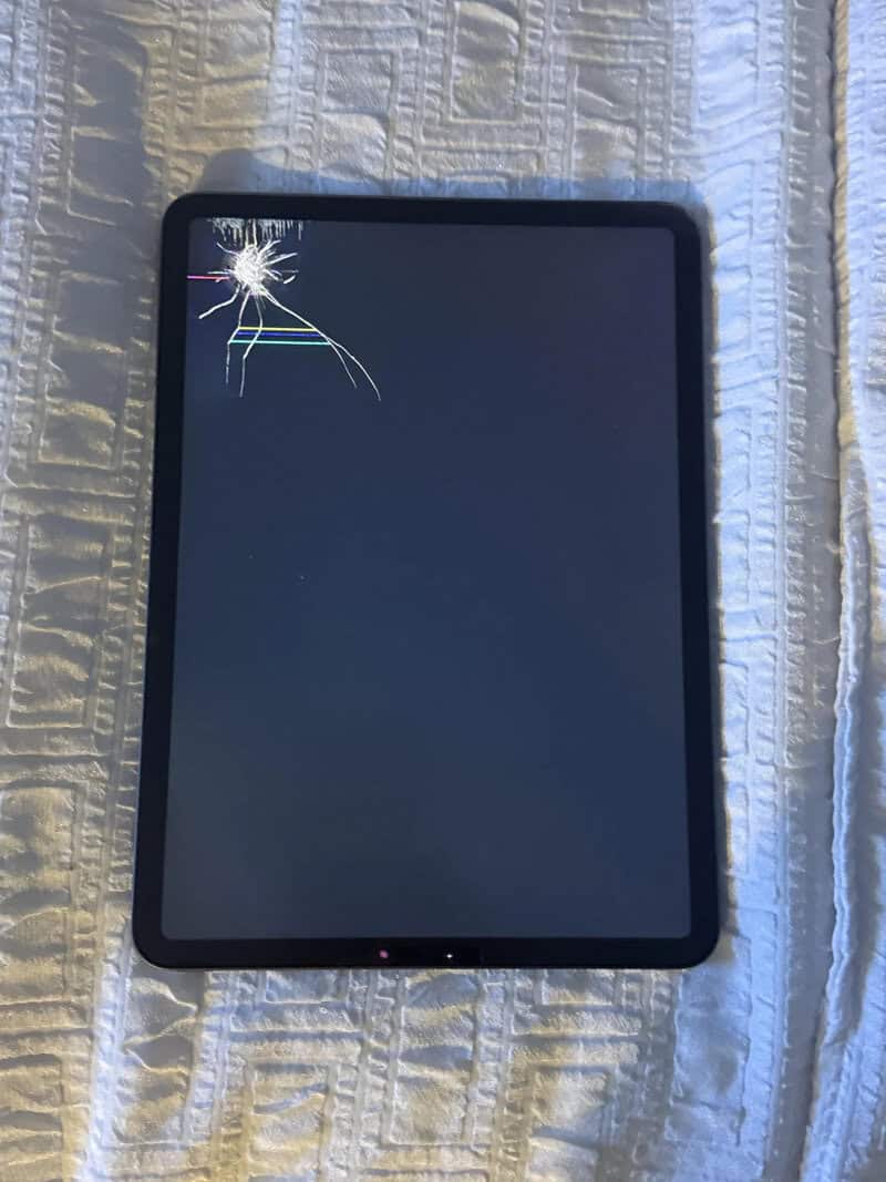 Tablet with a cracked screen on a white textured surface.