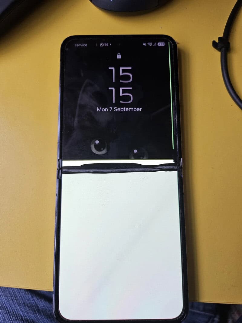 Folded smartphone with a white screen on a yellow surface.
