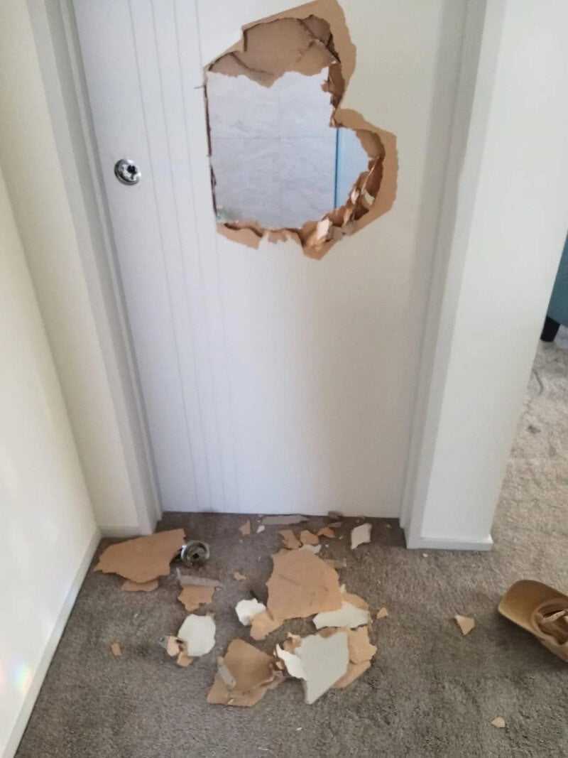 Hole in door with debris on floor, part of wall damaged.